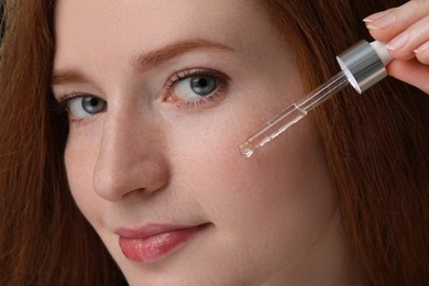 Photo of Beautiful woman with freckles applying cosmetic serum onto her face, closeup