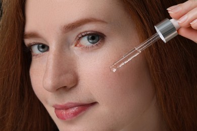 Beautiful woman with freckles applying cosmetic serum onto her face, closeup