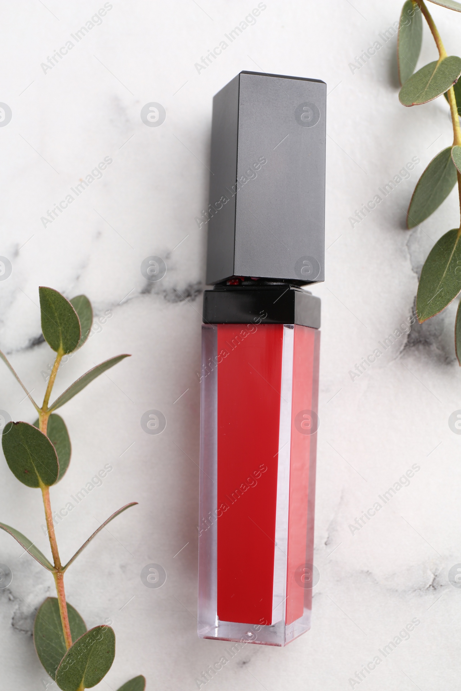 Photo of Red lip gloss and green leaves on white marble table, flat lay