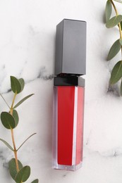 Red lip gloss and green leaves on white marble table, flat lay