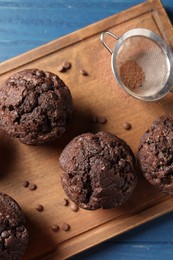 Delicious chocolate muffins and sieve with cocoa powder on blue wooden table, top view