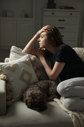 Sad young woman and her dog on sofa at home