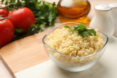 Delicious bulgur with parsley in bowl and products on table, closeup