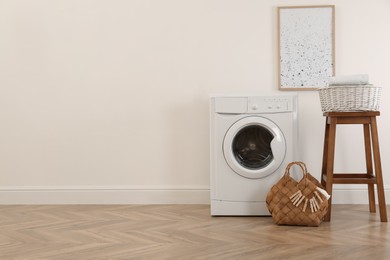 Photo of Laundry room interior with modern washing machine and wooden stool near white wall. Space for text