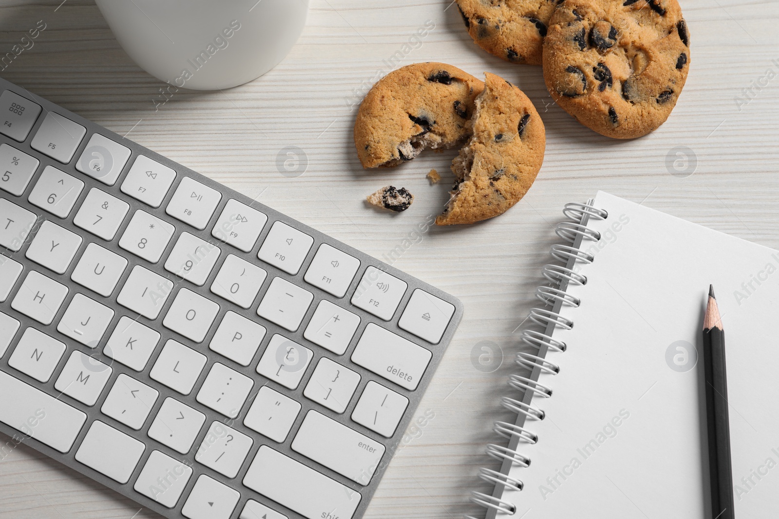 Photo of Chocolate chip cookies, keyboard and office supplies on white wooden table, flat lay