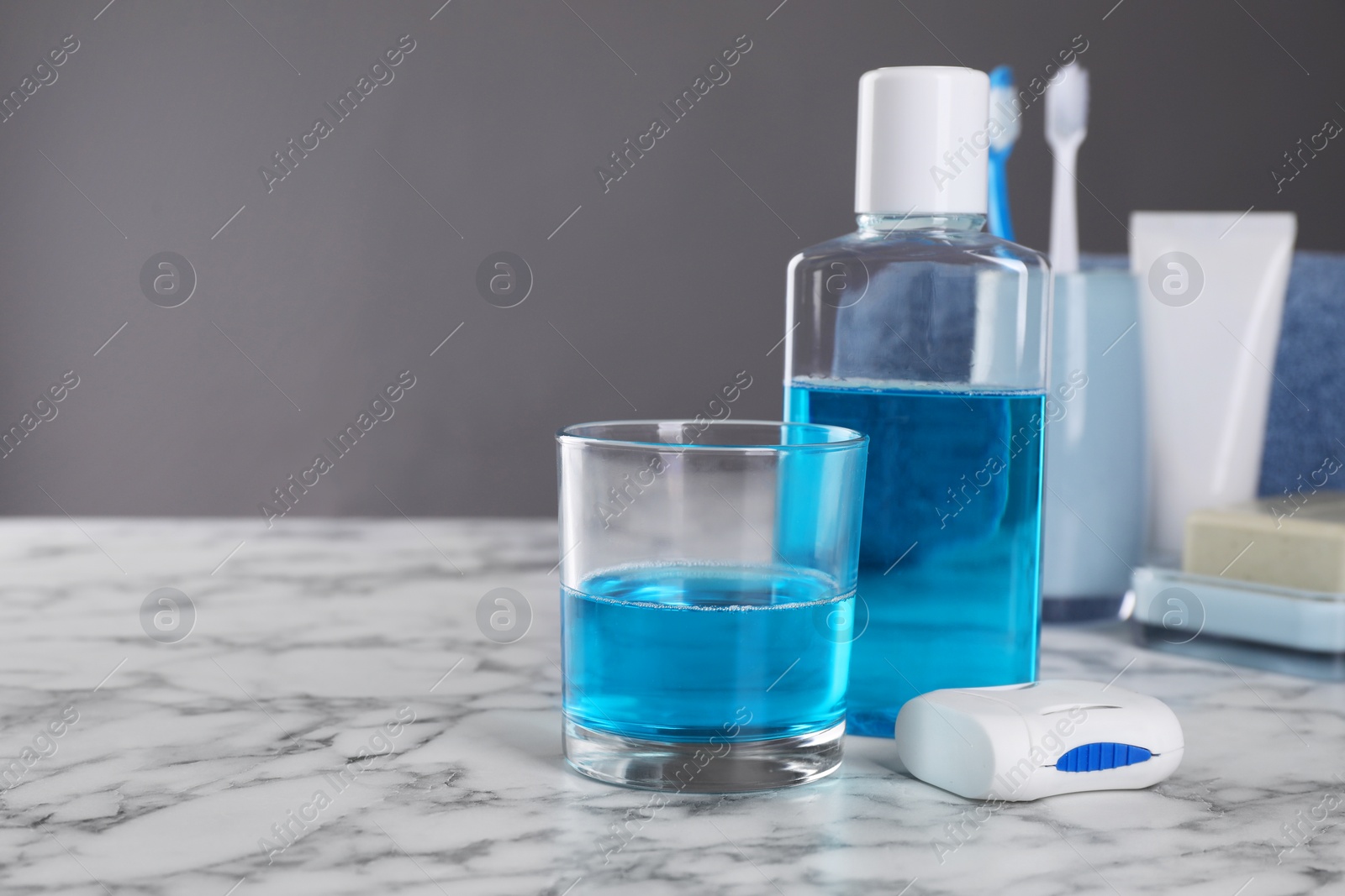 Photo of Fresh mouthwash in bottle, glass and dental floss on white marble table. Space for text