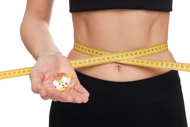 Photo of Slim woman holding pills and measuring waist with tape on white background, closeup. Weight loss