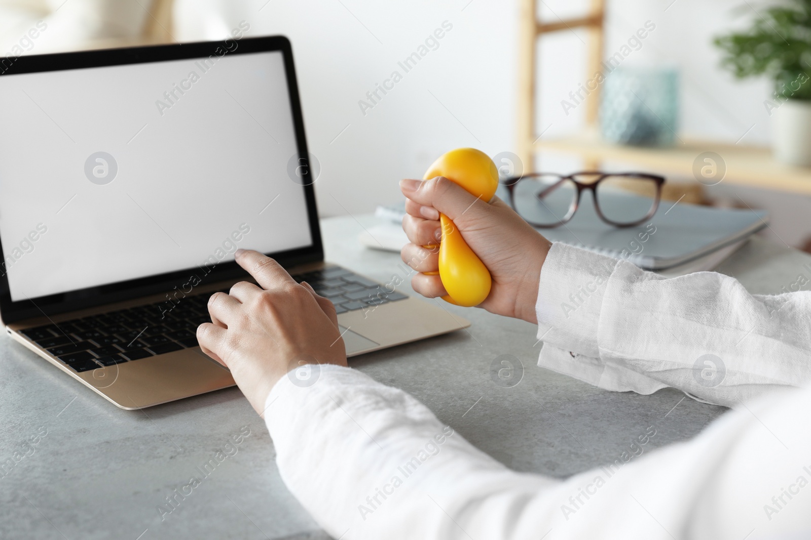 Photo of Woman squeezing antistress ball while working on laptop in office, closeup