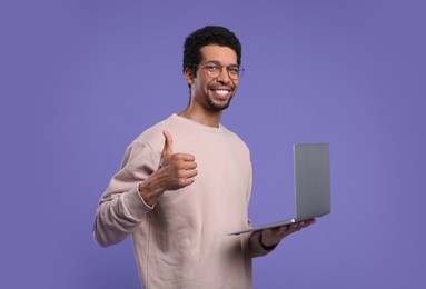 Photo of Smiling man with laptop showing thumb up on purple background