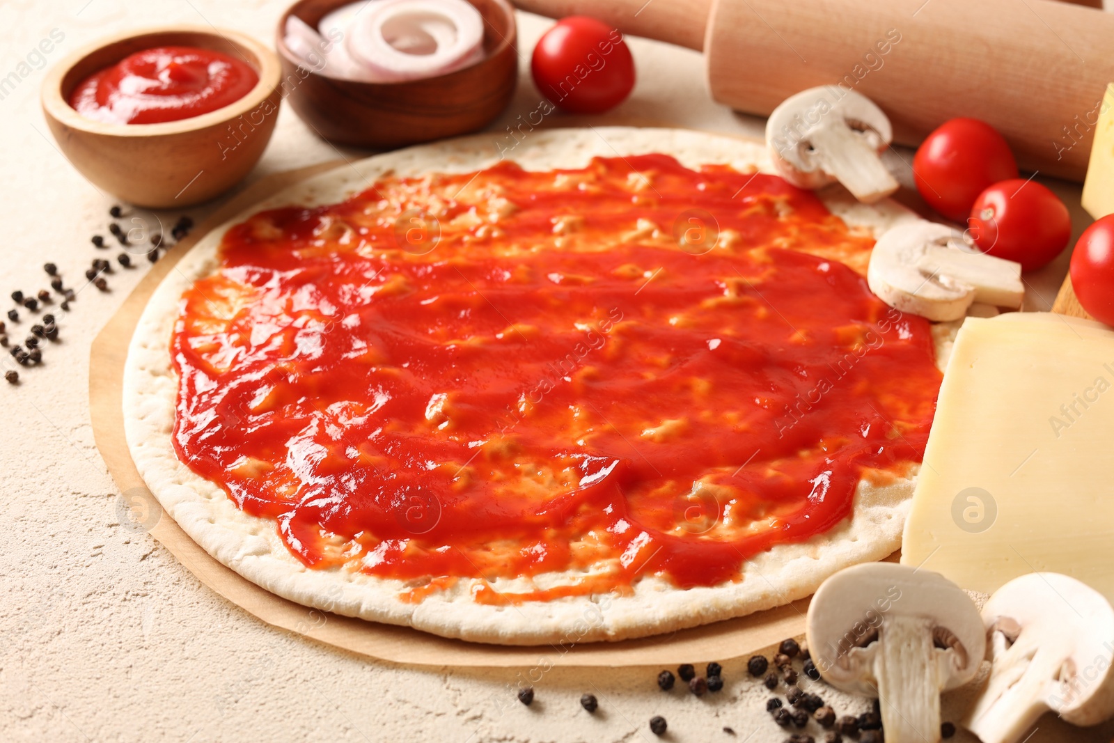 Photo of Pizza base smeared with tomato sauce, peppercorns and products on light textured table, closeup