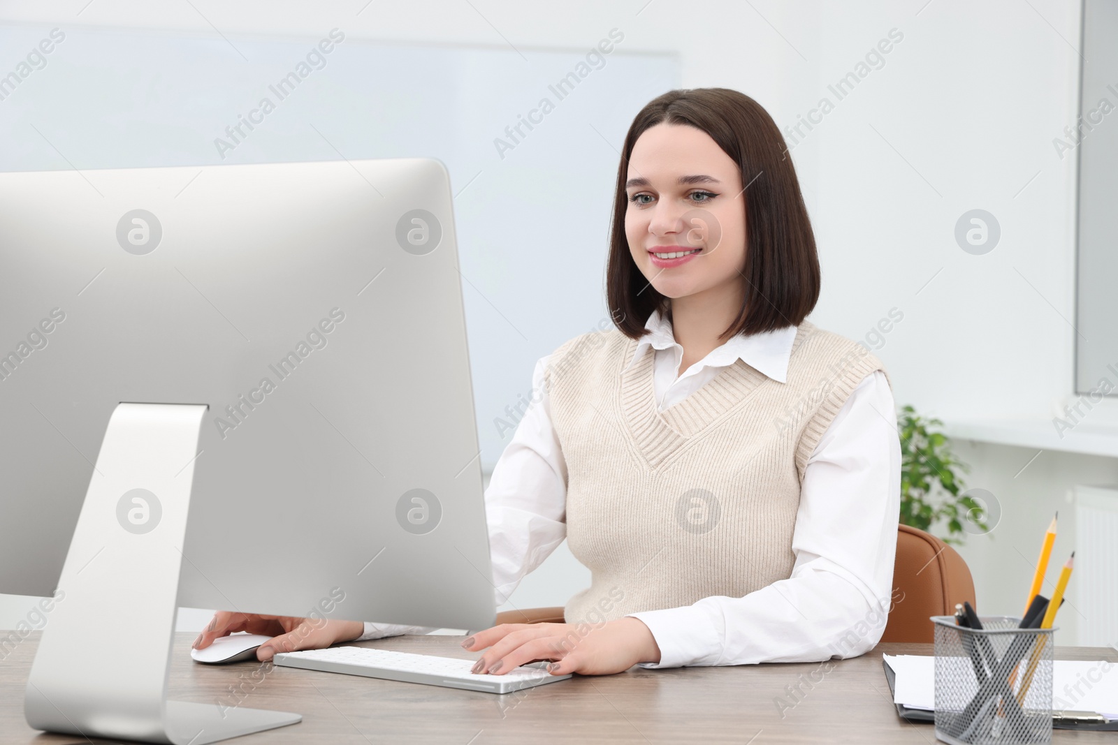 Photo of Happy young intern working with computer at table in modern office