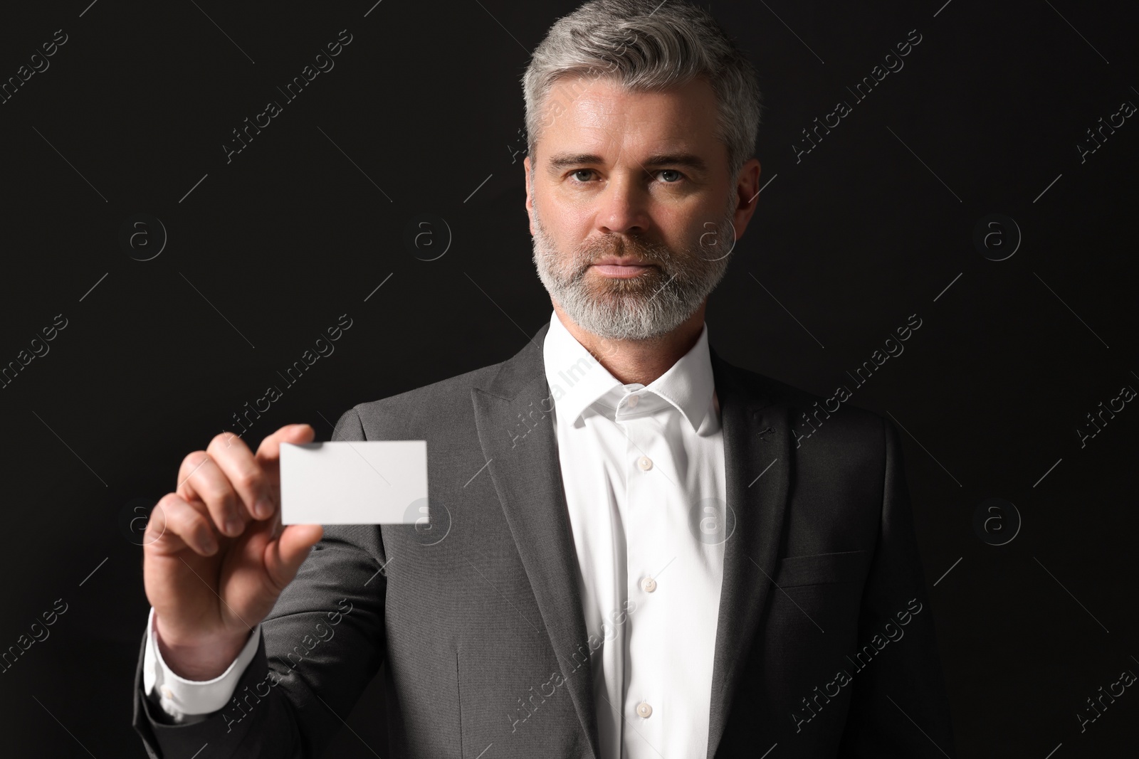 Photo of Handsome businessman holding blank business card on black background