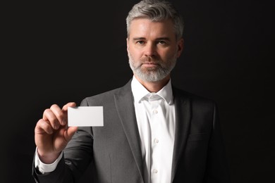 Handsome businessman holding blank business card on black background