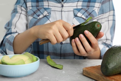 Photo of Woman peeling ripe avocado at table, closeup