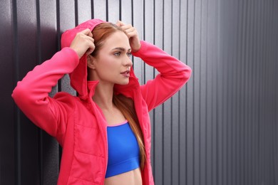 Beautiful woman in gym clothes posing near dark grey wall on street, space for text