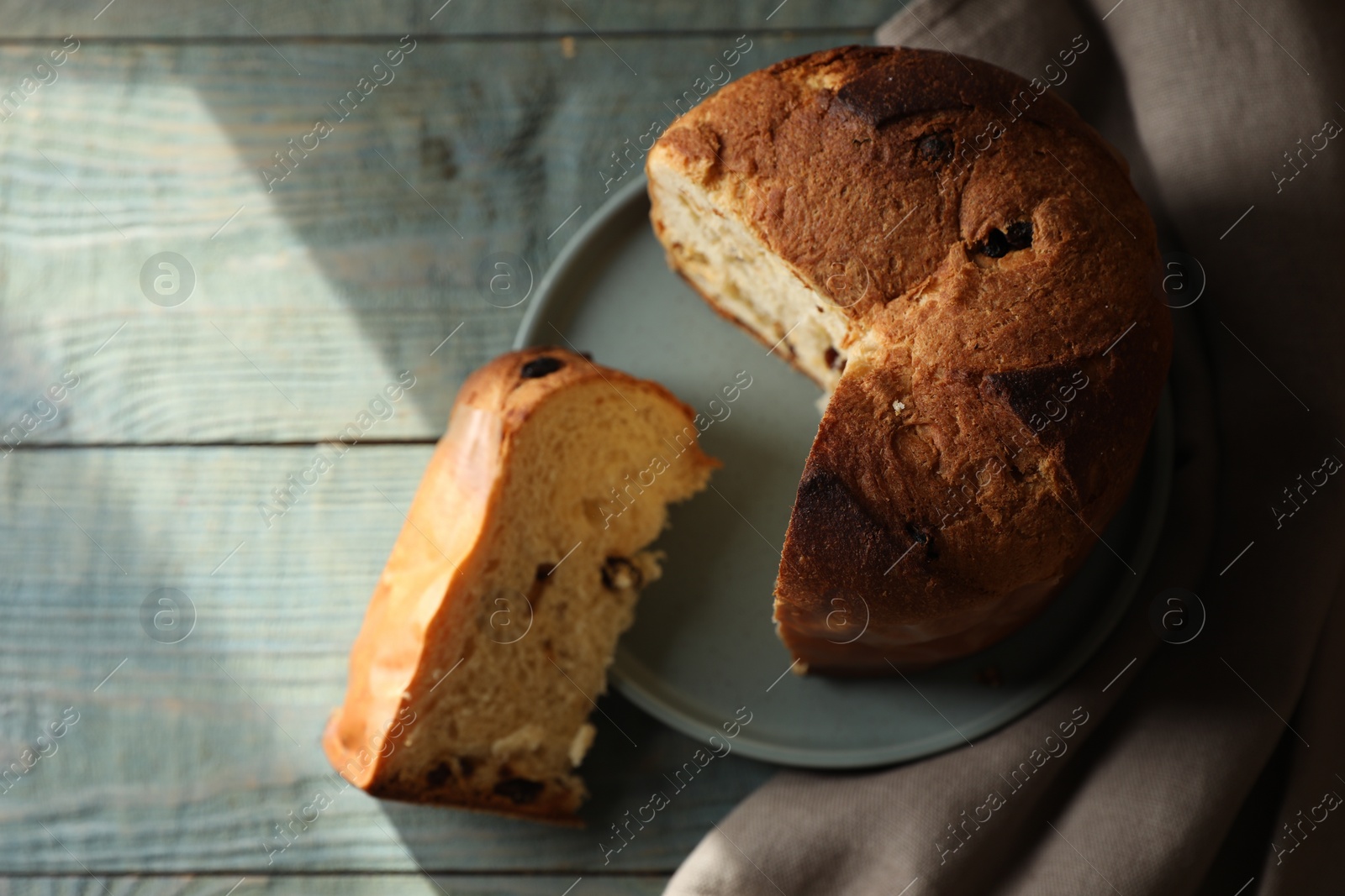 Photo of Delicious cut Panettone cake with raisins on light blue wooden table, flat lay. Traditional Italian pastry