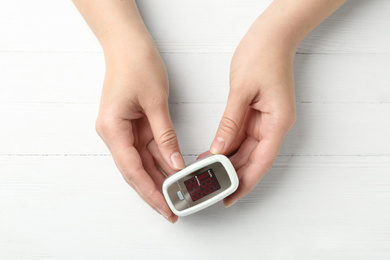 Photo of Woman holding fingertip pulse oximeter on white wooden background, top view