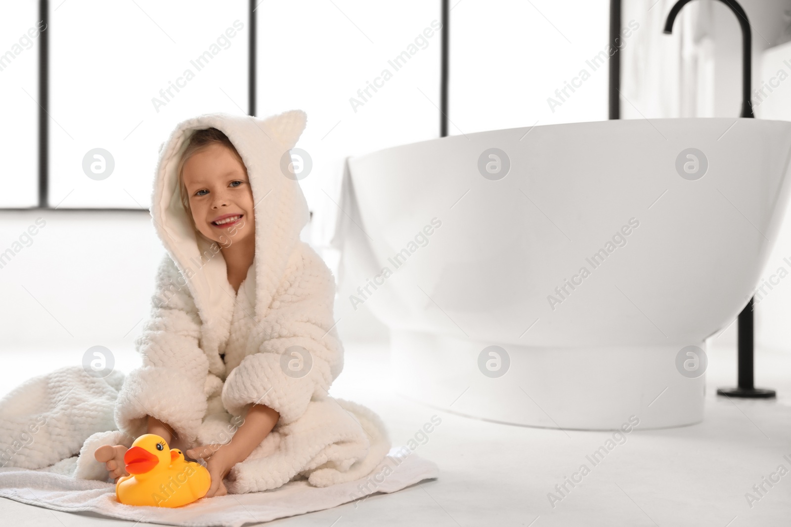 Photo of Cute little girl near tub in bathroom. Space for text