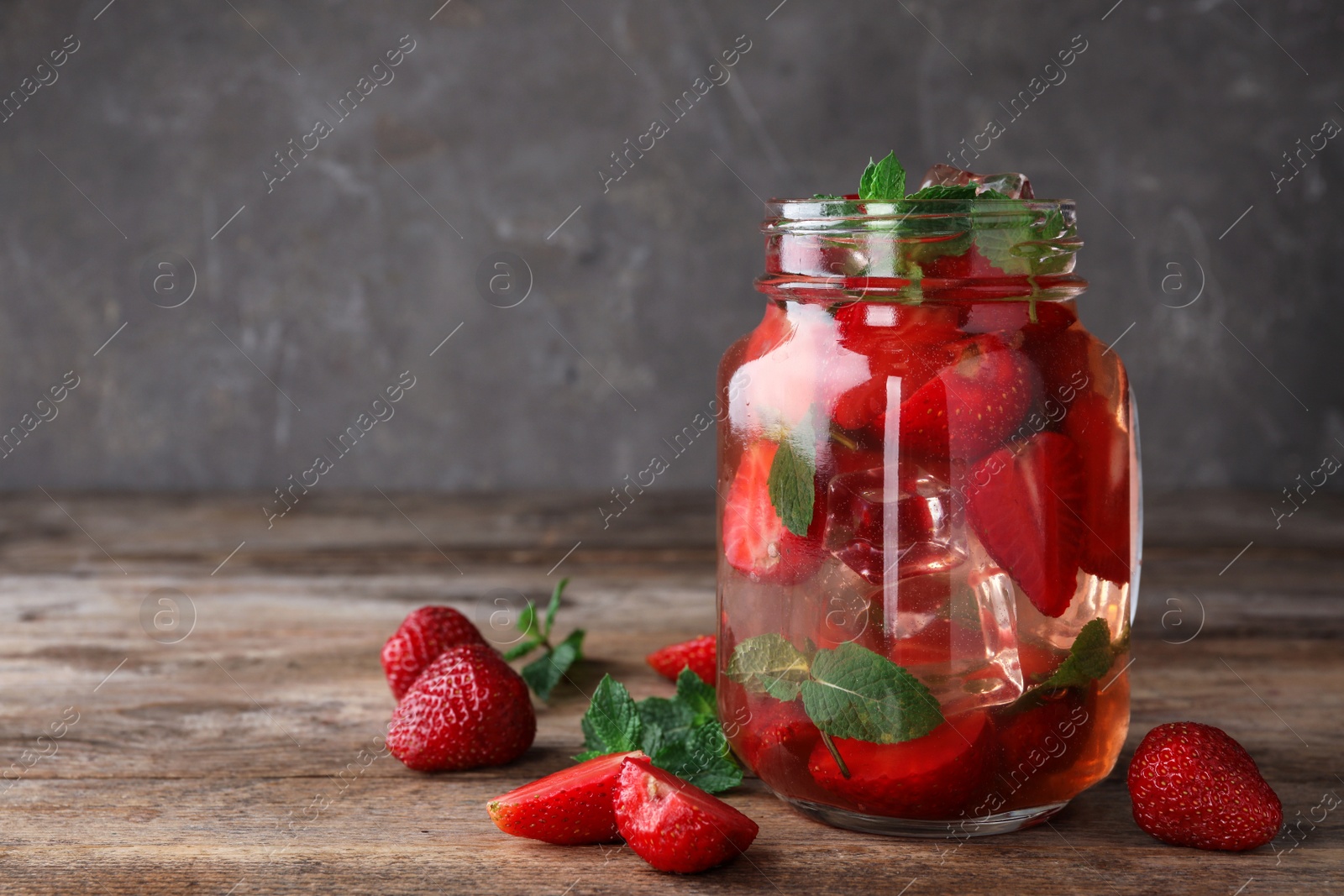 Photo of Mason jar of refreshing drink with strawberry and mint on wooden table against dark background, space for text