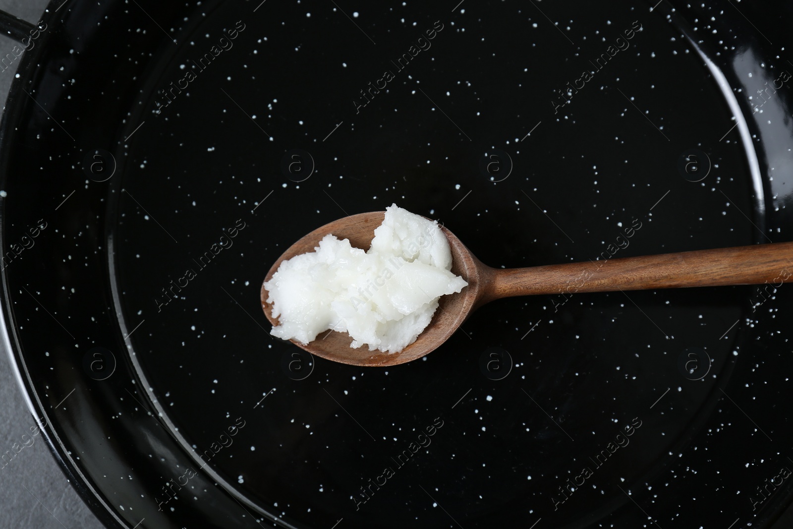 Photo of Frying pan with organic coconut cooking oil and wooden spoon, top view
