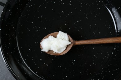 Frying pan with organic coconut cooking oil and wooden spoon, top view