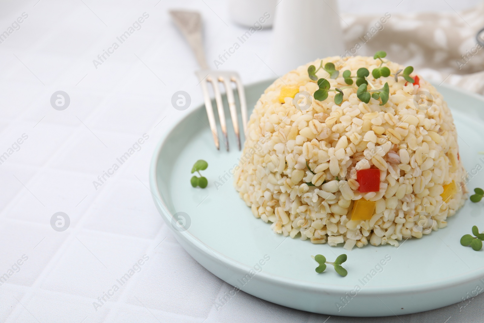 Photo of Delicious bulgur with vegetables and microgreens served on table, closeup. Space for text