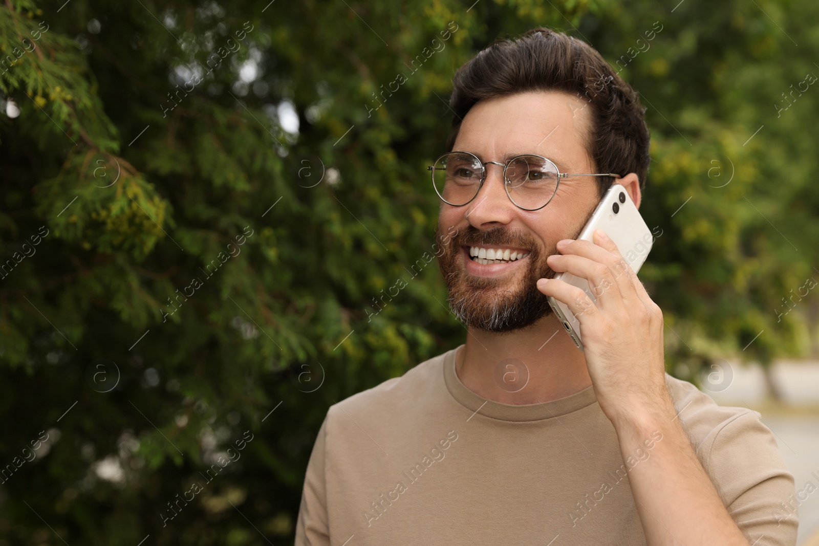 Photo of Smiling bearded man talking on phone outdoors. Space for text