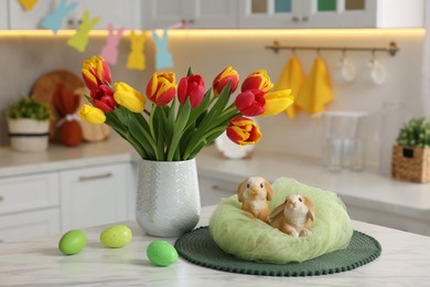Easter decorations. Bouquet of tulips, painted eggs and bunny figures on table indoors