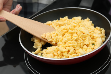 Woman cooking tasty scrambled eggs in frying pan on stove, closeup