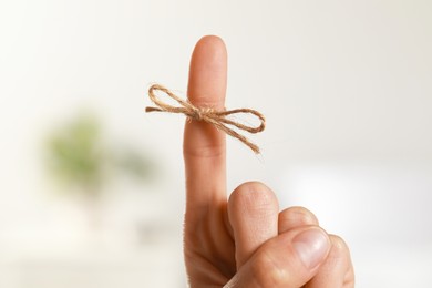 Woman showing index finger with tied bow as reminder on blurred background, closeup