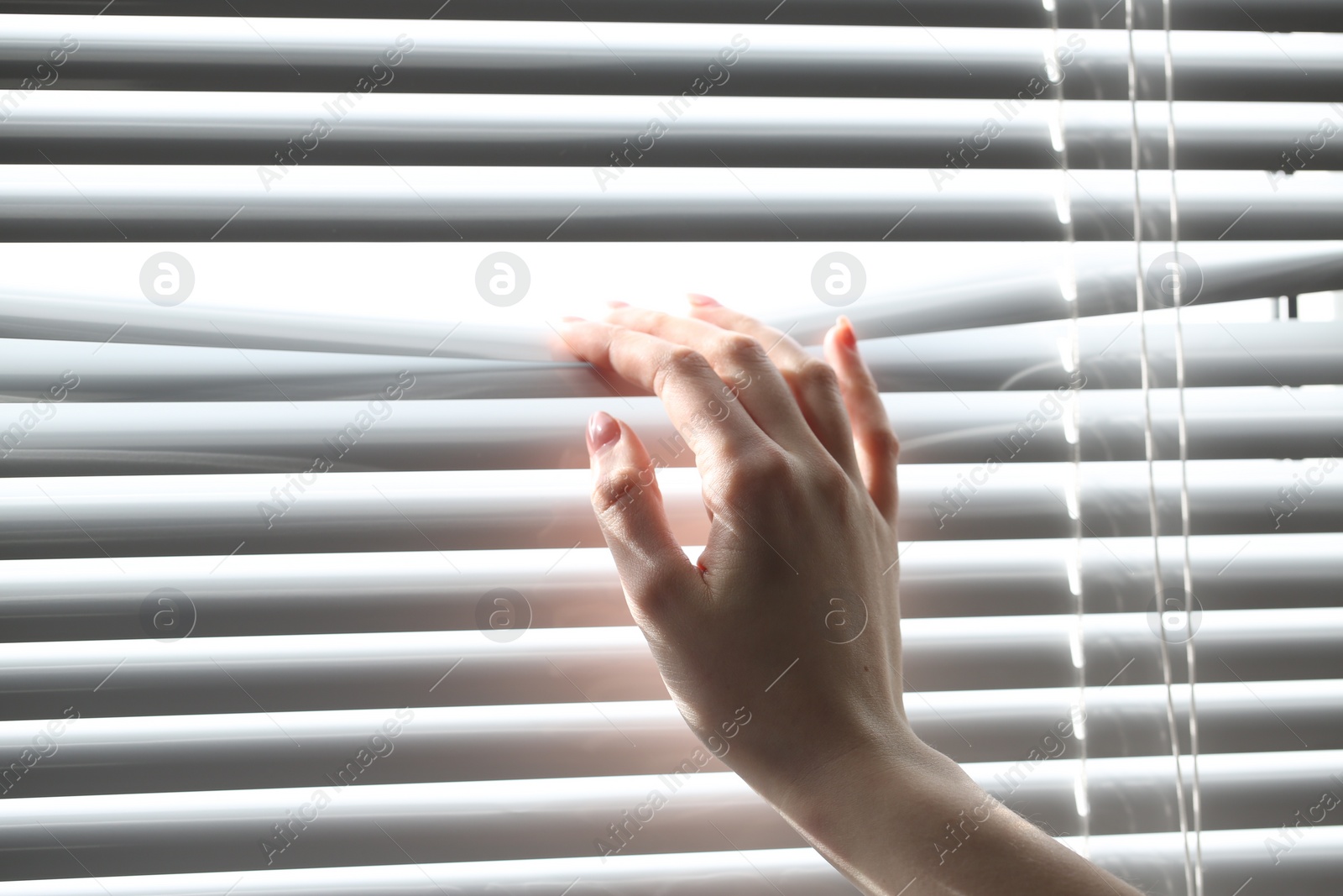 Photo of Woman separating slats of white blinds indoors, closeup