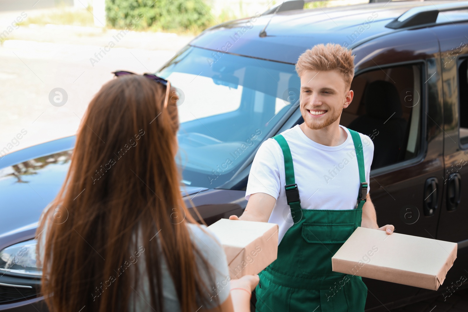 Photo of Young delivery courier giving parcels to customer outdoors