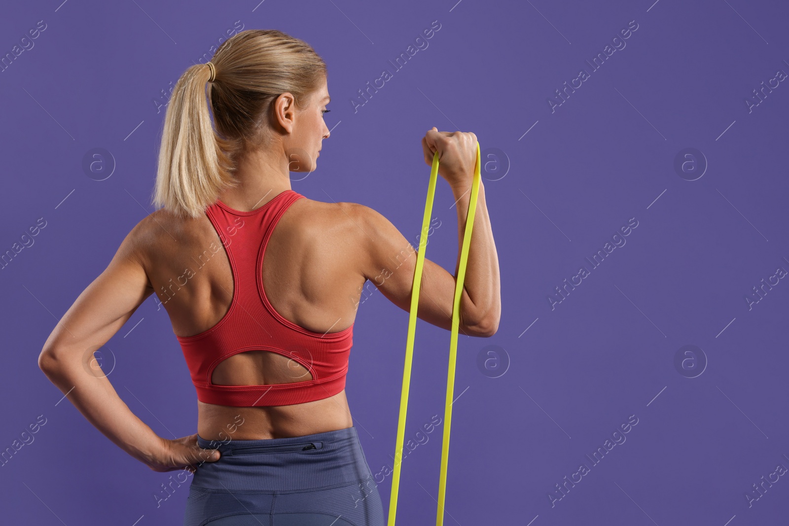 Photo of Athletic woman exercising with elastic resistance band on purple background, back view. Space for text