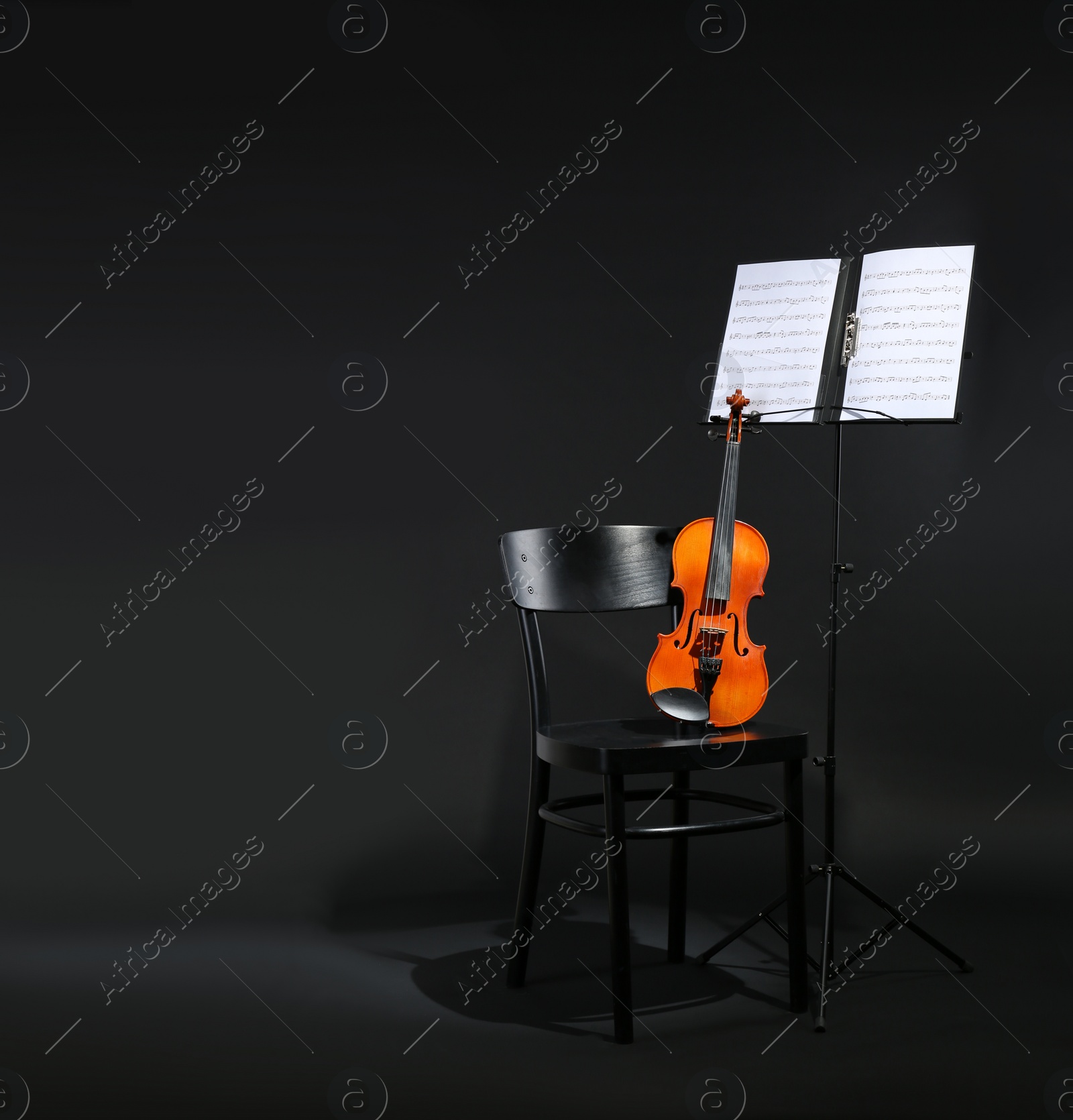 Photo of Violin, chair and note stand with music sheets on black background. Space for text