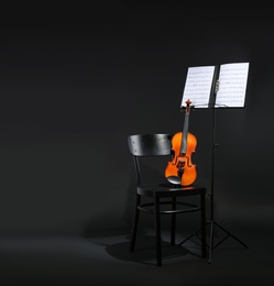 Photo of Violin, chair and note stand with music sheets on black background. Space for text