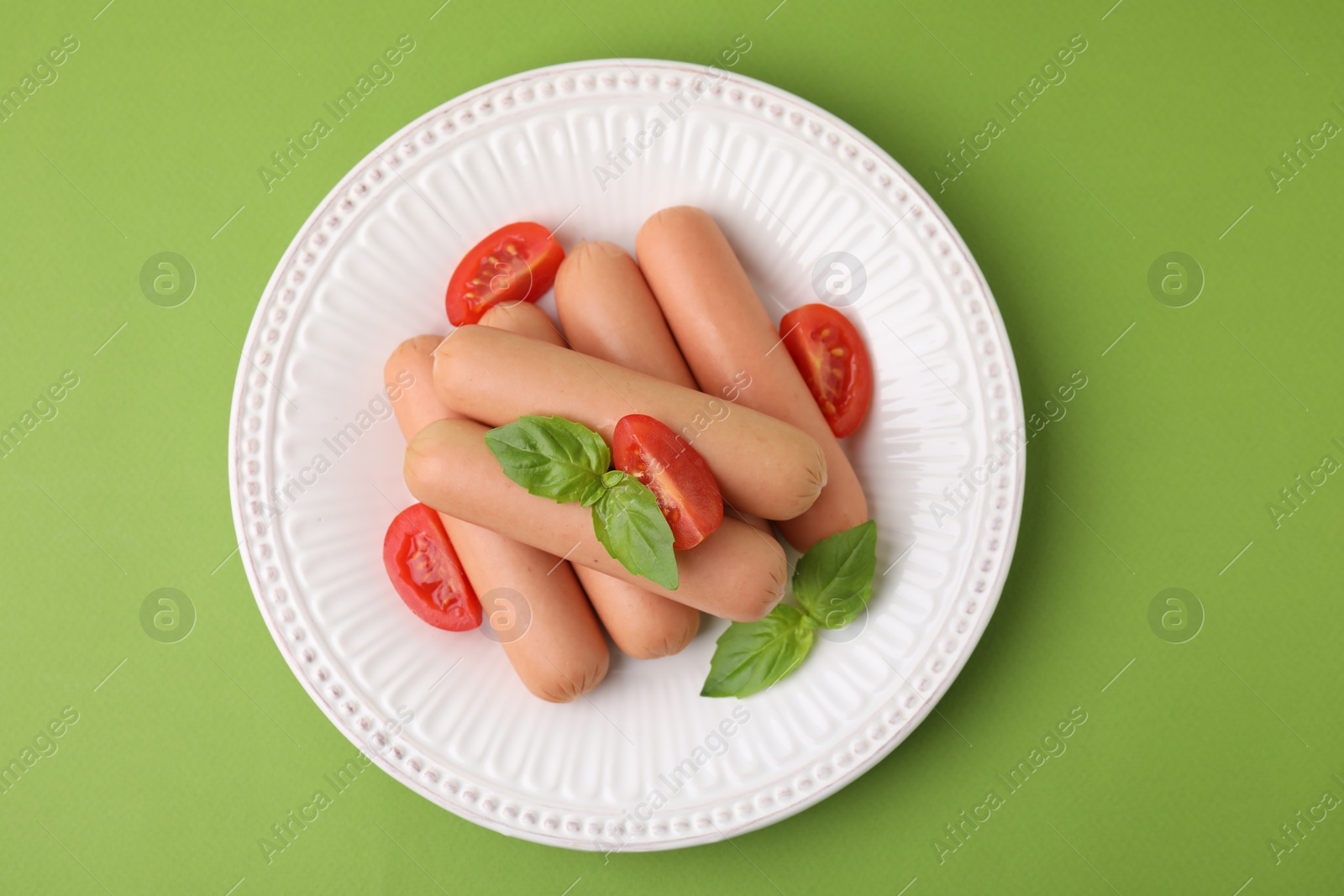 Photo of Delicious boiled sausages, tomatoes and basil on green table, top view