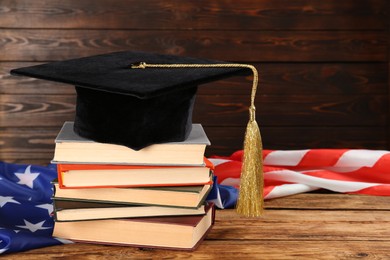 Photo of Graduation hat, books and American flag on wooden table. Space for text