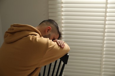 Photo of Sad man sitting on chair near window. Space for text