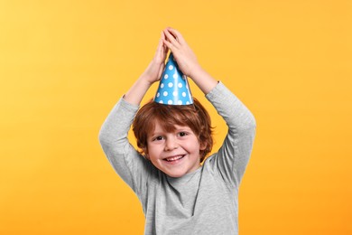 Photo of Birthday celebration. Cute little boy in party hat on orange background