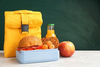 Lunch box with appetizing food and bag on table near chalkboard