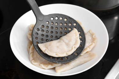 Photo of Delicious dumplings (varenyky) on skimmer over plate, closeup