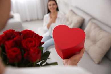 Photo of Man presenting gift and bouquet to his beloved woman at home, closeup. Valentine's day celebration