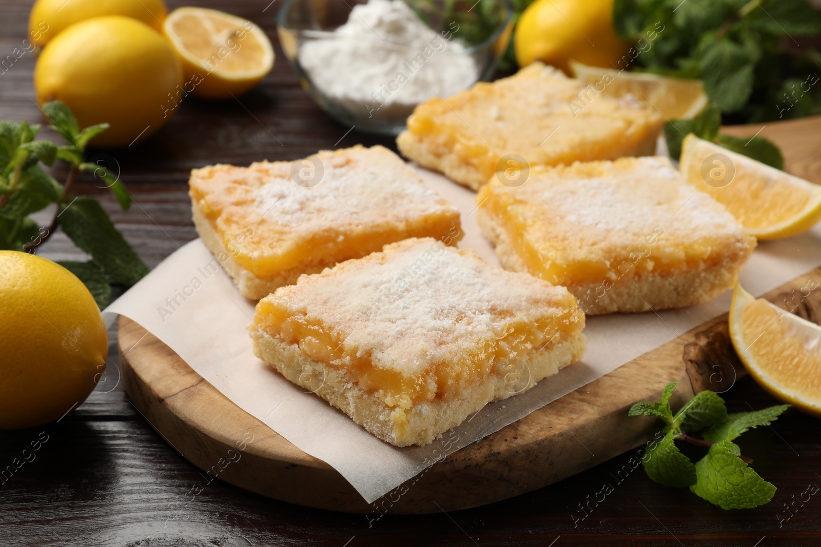 Photo of Tasty lemon bars with powdered sugar and mint on wooden table, closeup