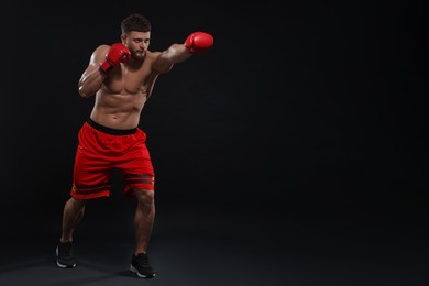 Man in boxing gloves fighting on black background. Space for text