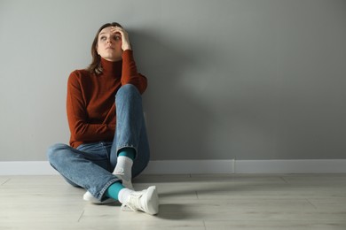 Photo of Sad young woman sitting on floor near grey wall indoors, space for text