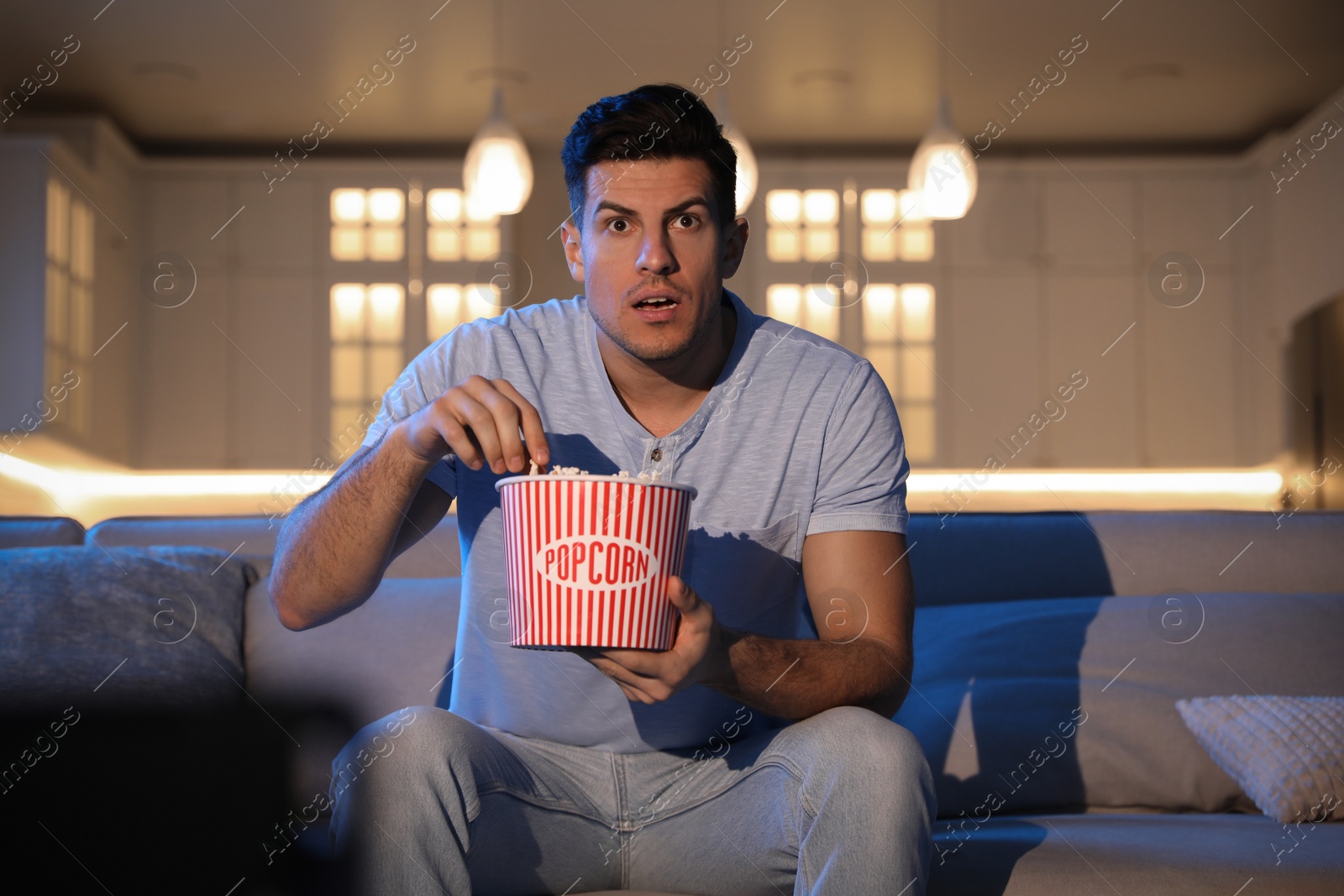 Photo of Man watching movie with popcorn on sofa at night