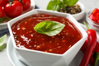 Photo of Spicy chili sauce with basil on light table, closeup