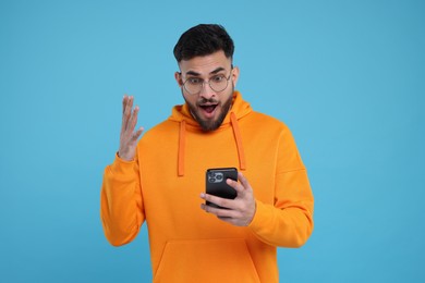 Photo of Shocked young man using smartphone on light blue background