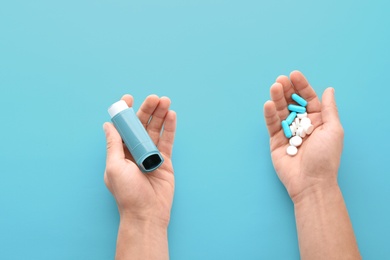 Photo of Man holding asthma inhaler and pills on blue background, top view