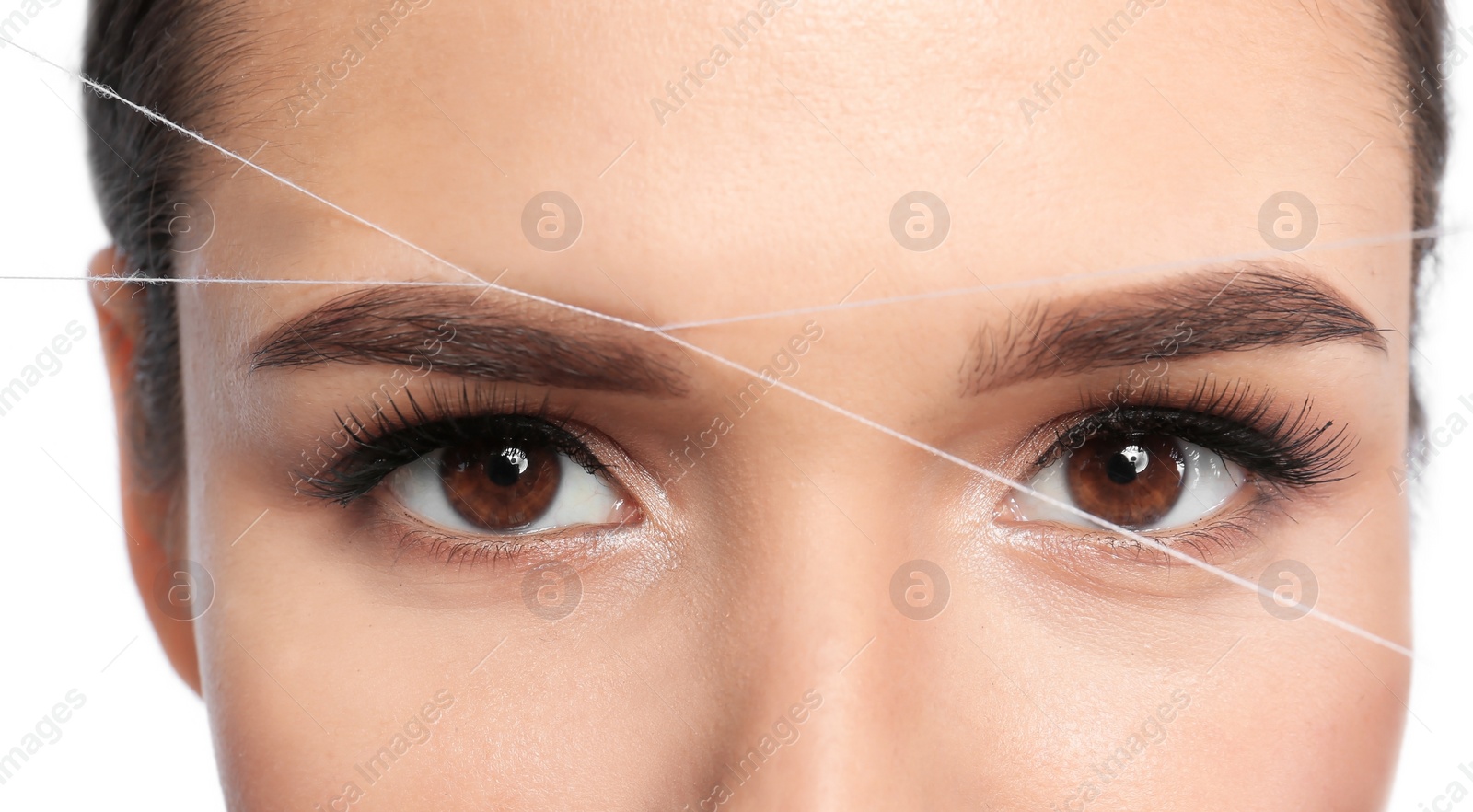 Photo of Young woman correcting eyebrow shape with thread, closeup